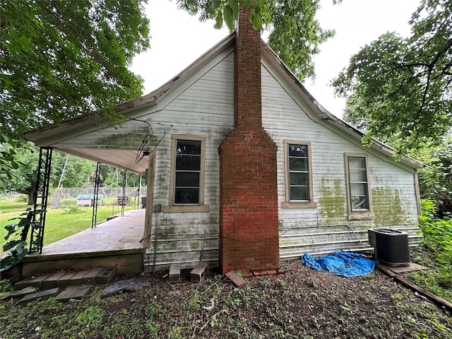 view of property exterior featuring a lawn, a patio, a chimney, and cooling unit
