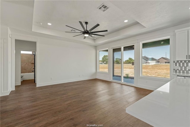 unfurnished living room featuring a ceiling fan, baseboards, dark wood-type flooring, a tray ceiling, and visible vents