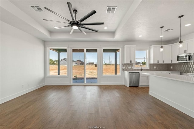 unfurnished living room with ceiling fan, a tray ceiling, dark wood-type flooring, and visible vents