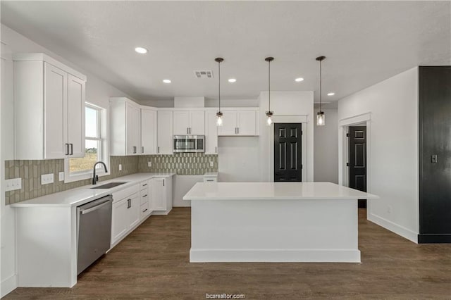 kitchen with appliances with stainless steel finishes, a sink, backsplash, a kitchen island, and visible vents
