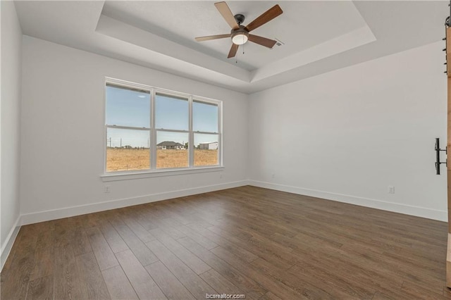 spare room with dark wood-style flooring, ceiling fan, baseboards, and a raised ceiling