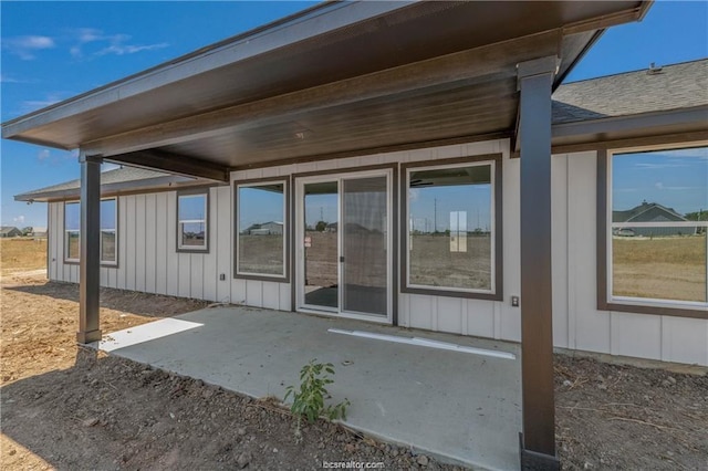 back of property with a shingled roof, board and batten siding, and a patio area
