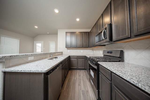 kitchen featuring light stone counters, a sink, appliances with stainless steel finishes, and dark brown cabinetry