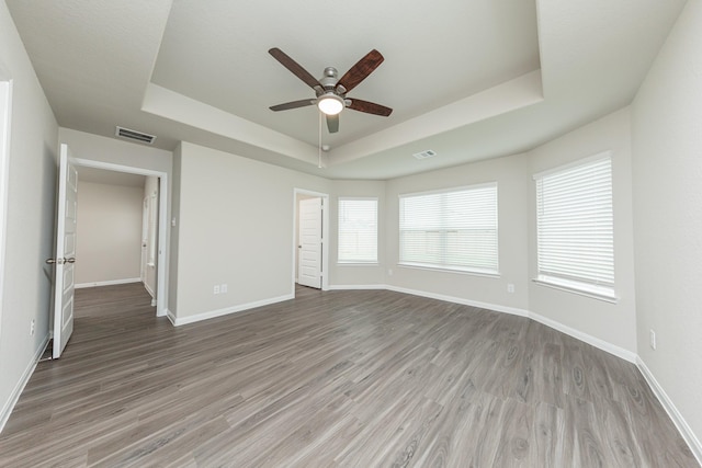 unfurnished bedroom featuring baseboards, visible vents, wood finished floors, and a raised ceiling