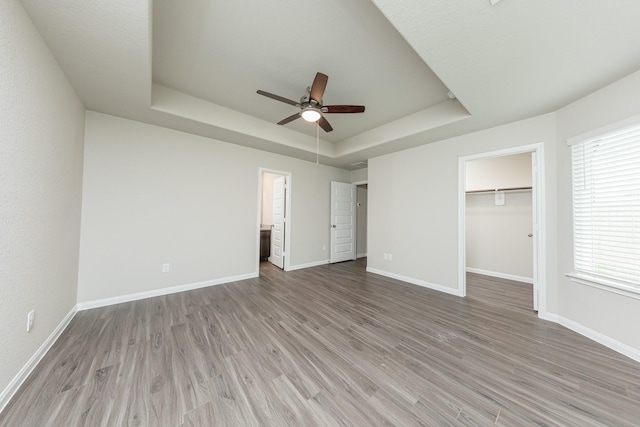 unfurnished bedroom with a raised ceiling, baseboards, wood finished floors, and a spacious closet