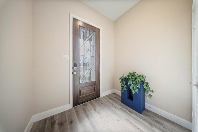 foyer featuring baseboards, wood finished floors, and lofted ceiling