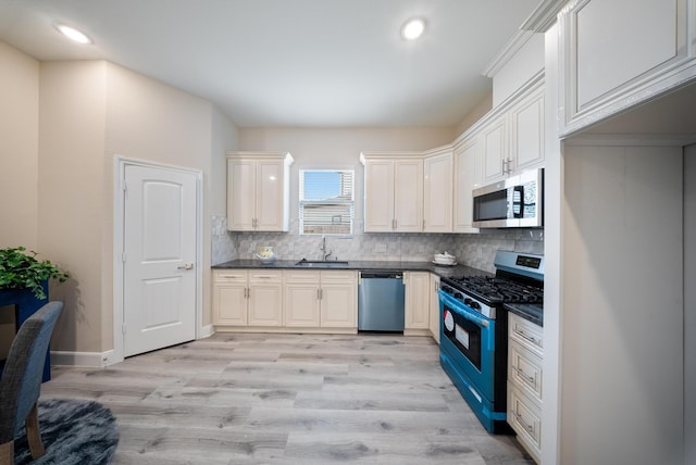 kitchen with dark countertops, a sink, light wood finished floors, appliances with stainless steel finishes, and backsplash