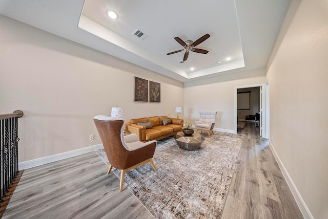 living room featuring ceiling fan, visible vents, light wood-type flooring, baseboards, and a tray ceiling