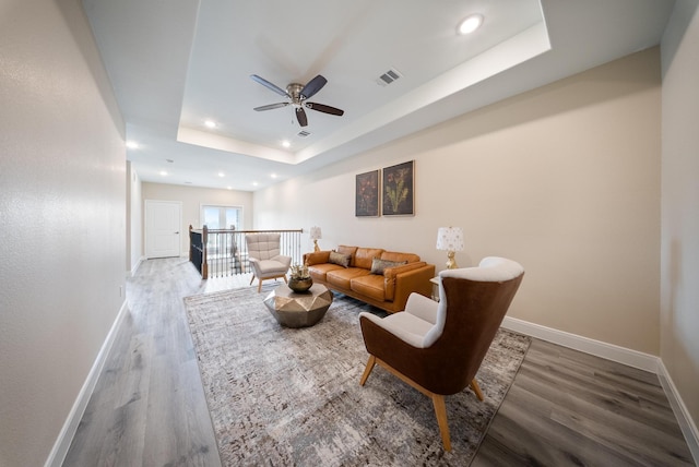 living room with visible vents, wood finished floors, baseboards, ceiling fan, and a tray ceiling