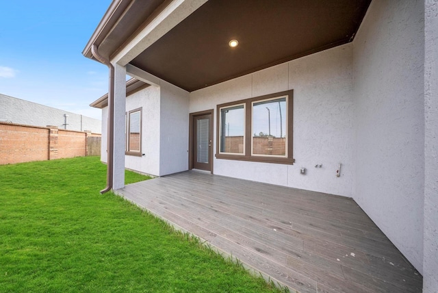 exterior space featuring fence, a wooden deck, stucco siding, and a yard