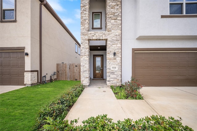 doorway to property featuring fence, an attached garage, stone siding, stucco siding, and a yard