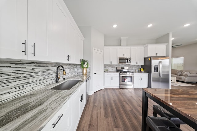 kitchen with light stone countertops, appliances with stainless steel finishes, a sink, white cabinetry, and tasteful backsplash