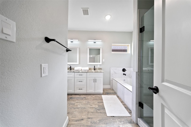 full bath with a textured wall, a sink, double vanity, wood finished floors, and a garden tub