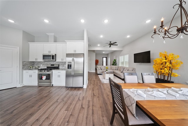 kitchen with decorative backsplash, dark wood finished floors, white cabinets, ceiling fan with notable chandelier, and stainless steel appliances