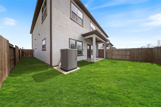 back of property with a yard, central AC, a fenced backyard, and stucco siding