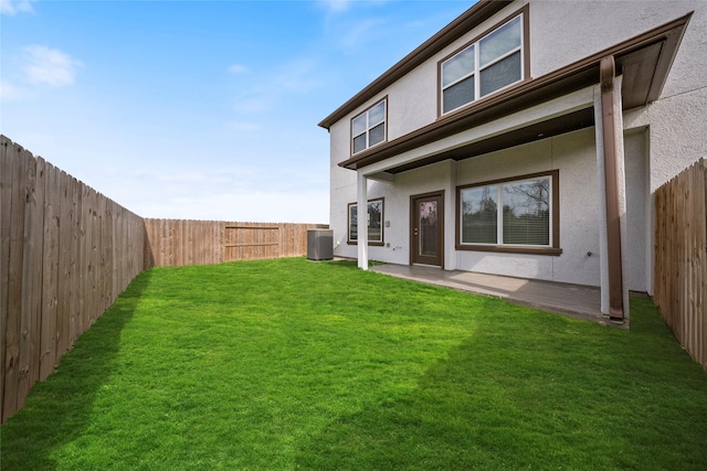 rear view of house featuring a yard, central AC unit, a fenced backyard, and stucco siding