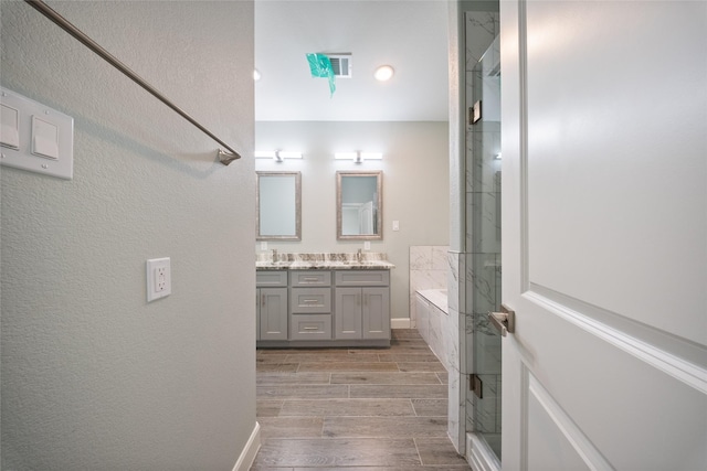 full bath with visible vents, double vanity, an enclosed shower, and wood finish floors