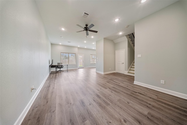 unfurnished living room featuring ceiling fan, baseboards, wood finished floors, visible vents, and stairway