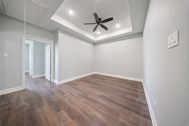 unfurnished room with dark wood-style flooring, attic access, recessed lighting, a tray ceiling, and a ceiling fan