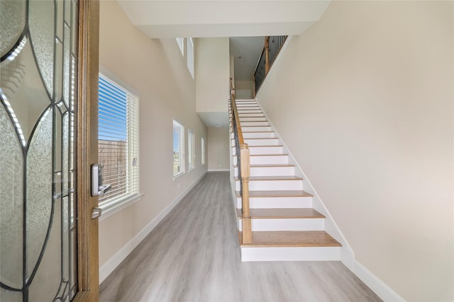 stairway with baseboards, wood finished floors, and a towering ceiling