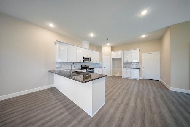 kitchen with a peninsula, baseboards, tasteful backsplash, a sink, and stainless steel appliances