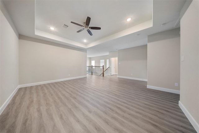unfurnished living room with visible vents, baseboards, a tray ceiling, a ceiling fan, and light wood-style flooring