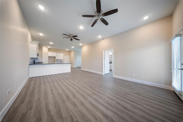 unfurnished living room with plenty of natural light, baseboards, ceiling fan, and wood finished floors