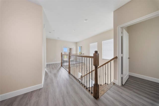 corridor featuring baseboards, wood finished floors, and an upstairs landing