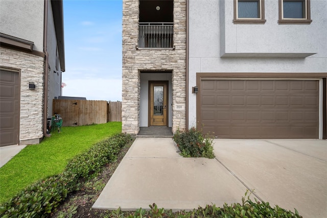 property entrance featuring driveway, fence, an attached garage, stone siding, and stucco siding