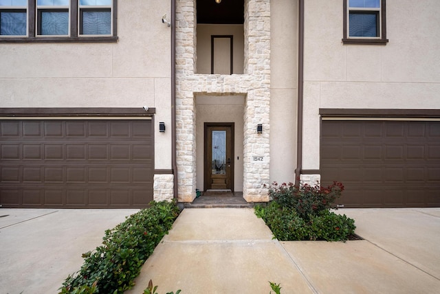 doorway to property featuring an attached garage, stucco siding, driveway, and stone siding