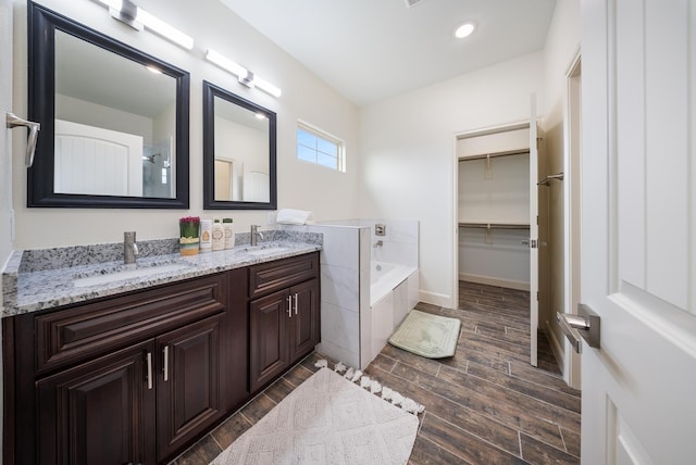 bathroom with a garden tub, a sink, and wood finished floors