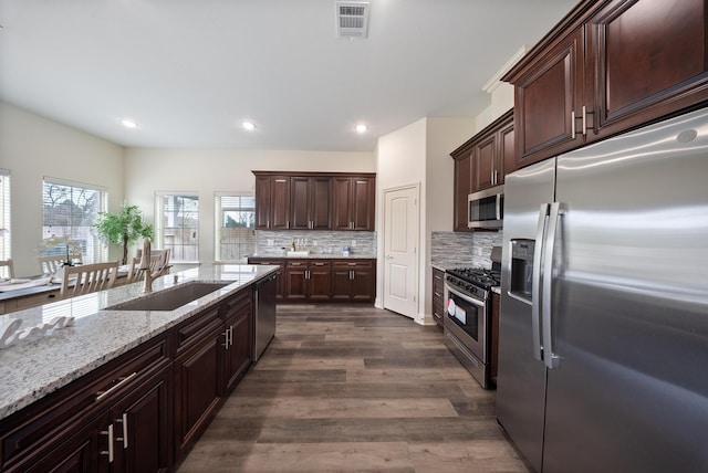 kitchen with light stone countertops, a sink, stainless steel appliances, tasteful backsplash, and visible vents