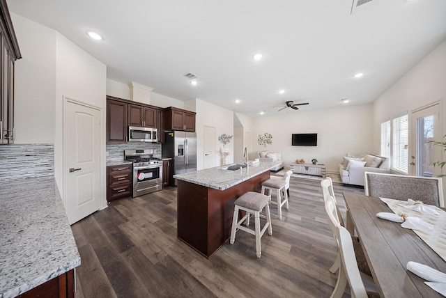 kitchen with appliances with stainless steel finishes, a sink, a ceiling fan, open floor plan, and tasteful backsplash