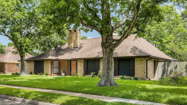 ranch-style home featuring a chimney, a front yard, roof with shingles, brick siding, and fence