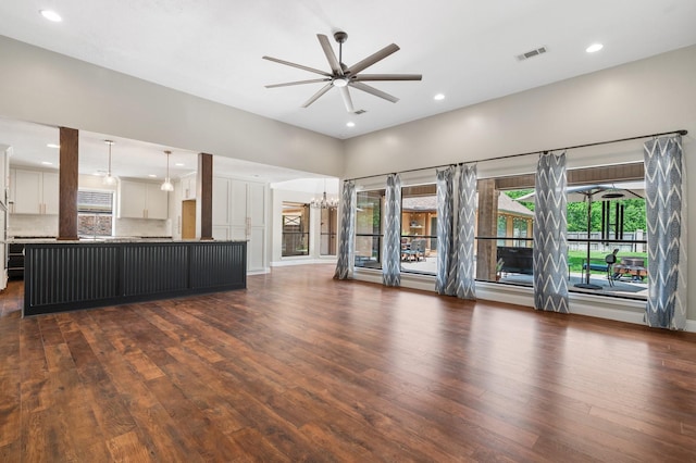 unfurnished living room with ceiling fan with notable chandelier, recessed lighting, baseboards, dark wood-type flooring, and visible vents