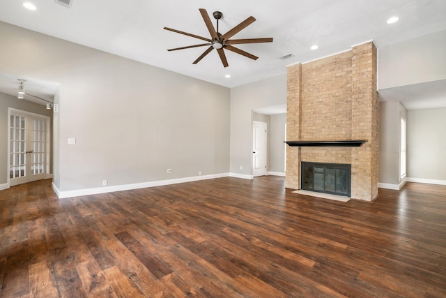 unfurnished living room featuring a brick fireplace, ceiling fan, visible vents, and dark wood-type flooring