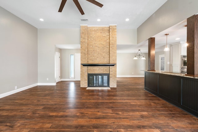 unfurnished living room with visible vents, dark wood-style flooring, a brick fireplace, baseboards, and a ceiling fan