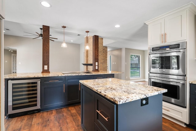 kitchen with ceiling fan, a kitchen island, stainless steel double oven, beverage cooler, and white cabinetry