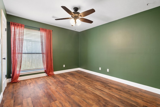 empty room featuring baseboards, ceiling fan, dark wood finished floors, and a wealth of natural light