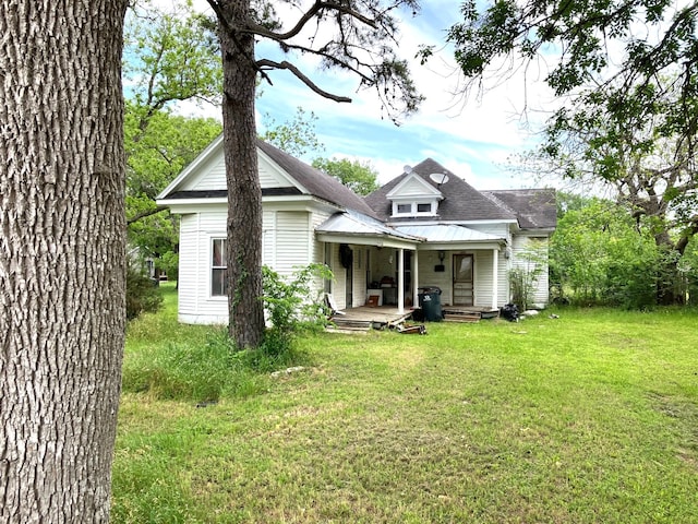 back of house featuring covered porch, a yard, metal roof, and roof with shingles