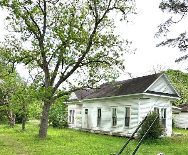 rear view of property with roof with shingles and a yard