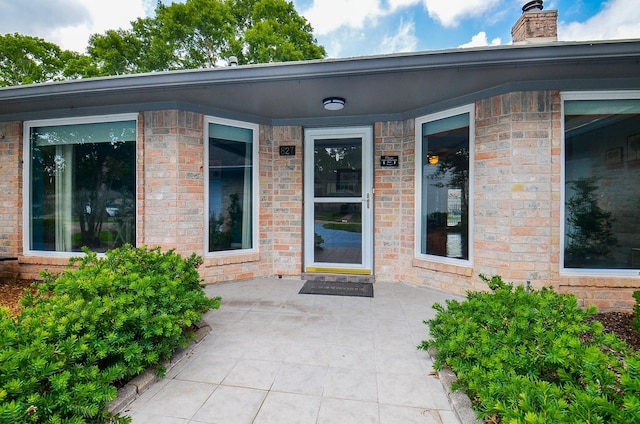 view of exterior entry with a chimney, a patio, and brick siding
