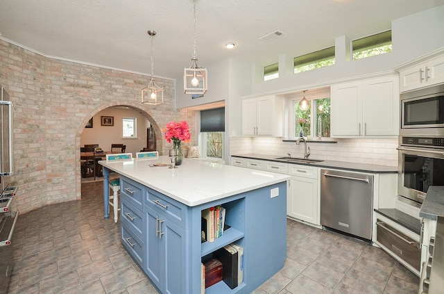 kitchen with appliances with stainless steel finishes, a sink, arched walkways, white cabinets, and brick wall