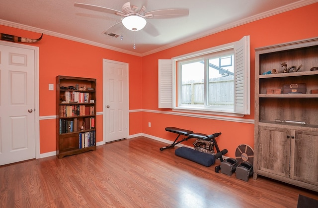 workout area featuring wood finished floors, a ceiling fan, ornamental molding, and baseboards