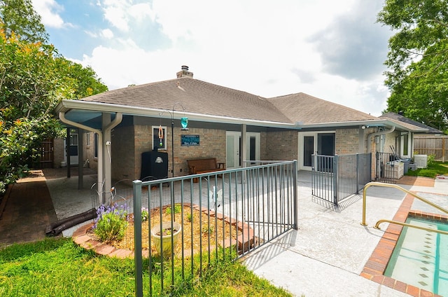 rear view of house featuring a patio, a chimney, fence, roof with shingles, and brick siding