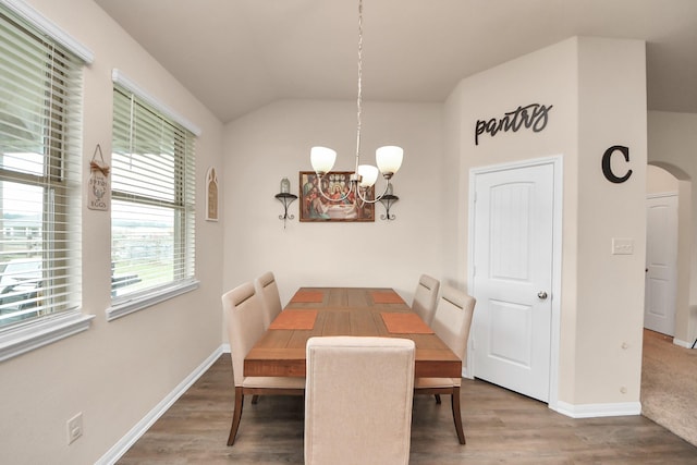 dining space with baseboards, lofted ceiling, wood finished floors, and a notable chandelier