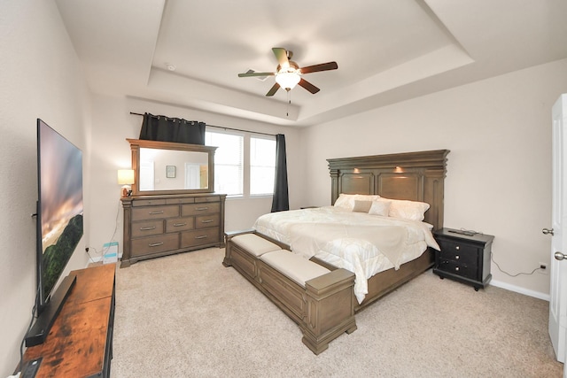 bedroom featuring a ceiling fan, a tray ceiling, light carpet, and baseboards
