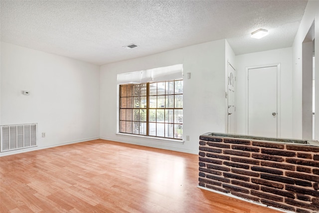 spare room featuring visible vents, baseboards, a textured ceiling, and wood finished floors