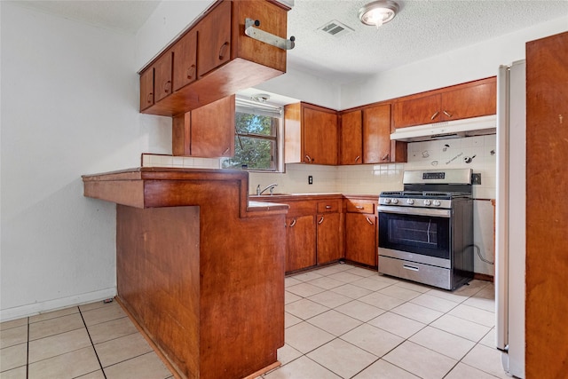 kitchen featuring decorative backsplash, brown cabinetry, visible vents, stainless steel gas range, and under cabinet range hood