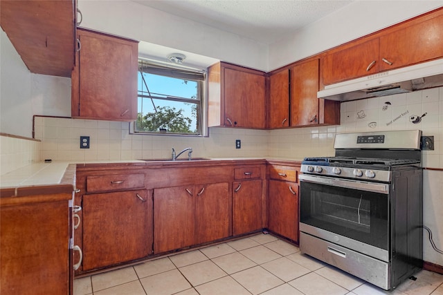kitchen featuring decorative backsplash, stainless steel range with gas stovetop, a sink, tile counters, and under cabinet range hood